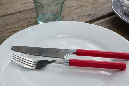 Close-up of plate with fork, butter knife and glass on wooden tableの写真素材