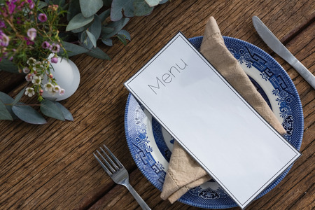 Close-up of plate with fork, butter knife, napkin and menu card on wooden tableの写真素材