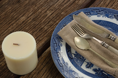 Close-up of cutlery and napkin on plate with candle