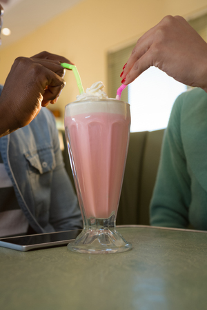 Close-up of couple holding drinking straw in milkshake at restaurantの写真素材