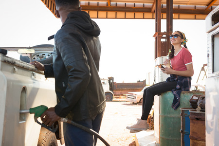 Man filling petrol in car while woman sitting at petrol pump station on a sunny dayの写真素材