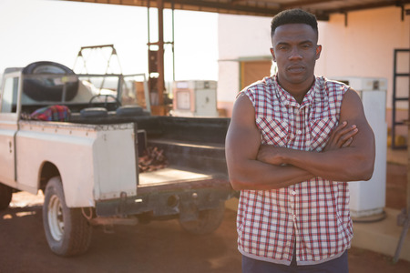 Man standing with arms crossed at petrol pump on a sunny dayの写真素材