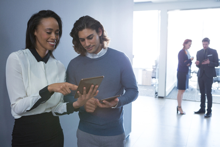 Male and female executives discussing over digital tablet in officeの写真素材