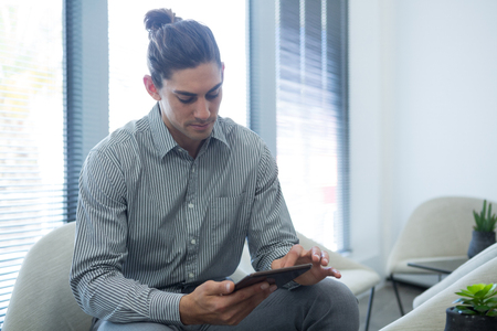 Male executive using digital tablet in waiting area of officeの写真素材
