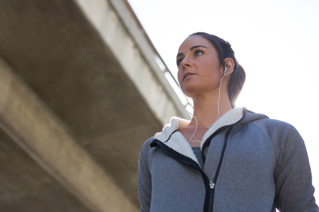 Thoughtful female jogger listening to music on a sunny dayの写真素材