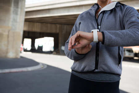 Mid section of female jogger using smartwatch on a sunny dayの写真素材
