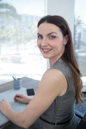 Portrait of confident female executive sitting at desk in officeの写真素材
