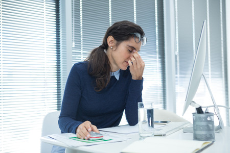 Tired female executive sitting at desk in officeの写真素材