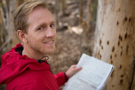 Portrait of young hiker man looking into camera while holding a map in the forest