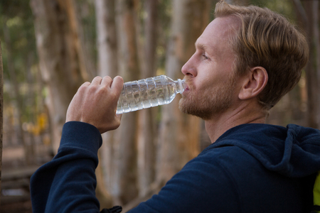 Athletic man drinking water from a bottle in the forest