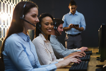 Business executives with headsets using computers at desk in officeの写真素材