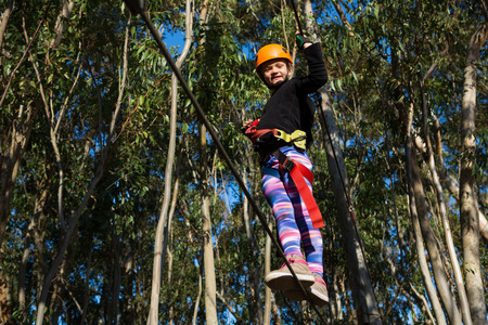 Little girl wearing helmet crossing zip line in the forest