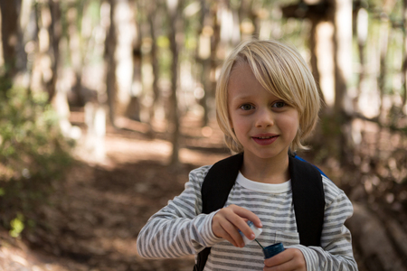 Portrait of little girl holding bubble wand in her hand in the forest on a sunny dayの写真素材