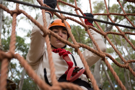 Close-up of woman wearing safety helmet climbing on a rope fence in the forest