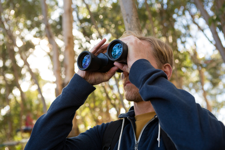 Man hiker exploring nature through binoculars in the forestの写真素材