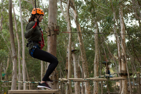 Young woman crossing through a zip line in the forest