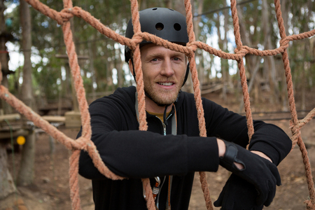 Portrait of man wearing safety helmet leaning on rope fence in the forest