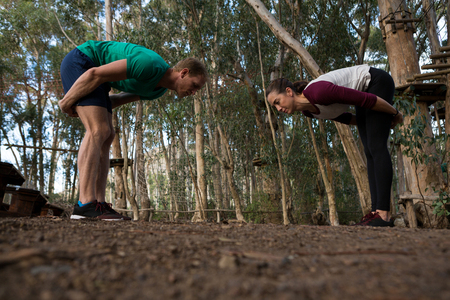 Woman performing bending exercise with her trainer in the forestの写真素材