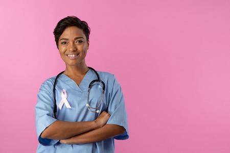 smiling nurse with crossed arms wearing pink ribbon om a pink backgroundの写真素材
