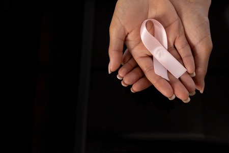 Hands presenting pink ribbon for breast cancer awareness on black backgroundの写真素材