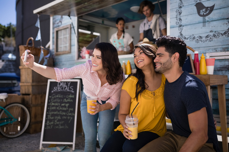 Happy friends taking selfie from mobile phone in food truck van