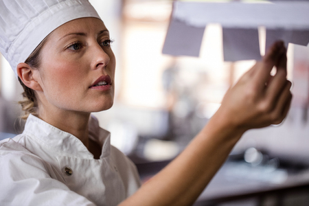 Female chef looking at order list in kitchen at hotelの写真素材