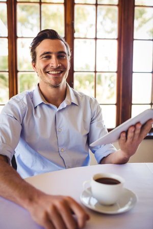 Smiling man using digital tablet while having coffee in restaurantの写真素材