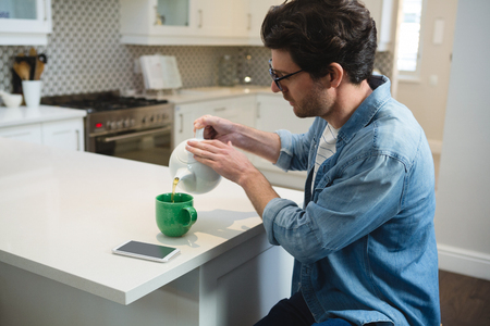 Young man pouring lemon tea into mug at homeの写真素材