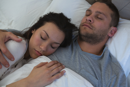 Couple sleeping on bed in bedroom at homeの写真素材