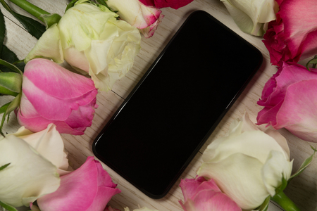 Close-up of mobile phone surrounded with rose flowerの写真素材
