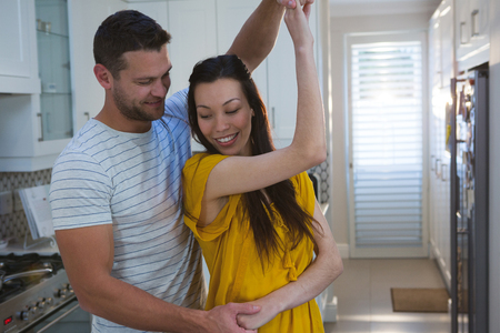 Couple dancing together in kitchen at homeの写真素材