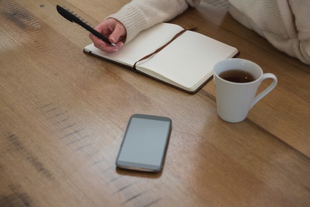 Mid section of woman writing on a diary at home