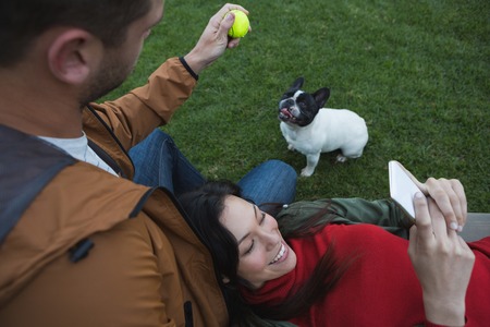 Man playing with his dog while woman using mobile phone in the park