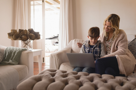 Front view of mother helping her son use laptop in stylish living room at homeの写真素材