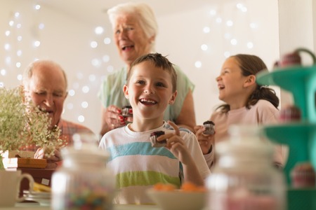 Happy multi-generation family eating cupcake at home for grandsons birthdayの写真素材
