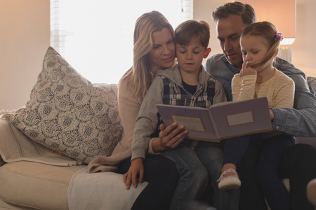 Front view of Caucasian family of four reading story book in living room at homeの写真素材