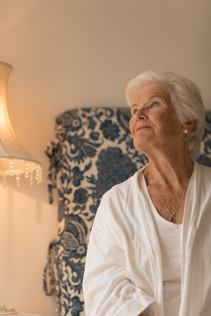 Front view of a senior woman looking up in her bedroom at homeの写真素材