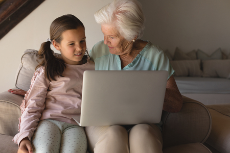 Front view of a grandmother and granddaughter discussing over laptop in living room at homeの写真素材