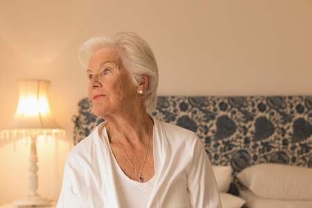 Front view of a depressed senior woman looking away and relaxing in bedroom at home