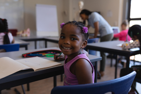 Rear view smiling schoolgirl sitting at desk and looking at camera in classroom of elementary school