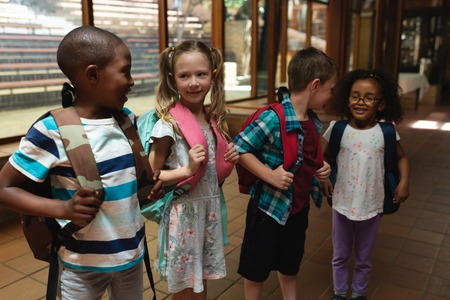 Front view of schoolkids talking with each other with theirs schoolbags in corridor of elementary...