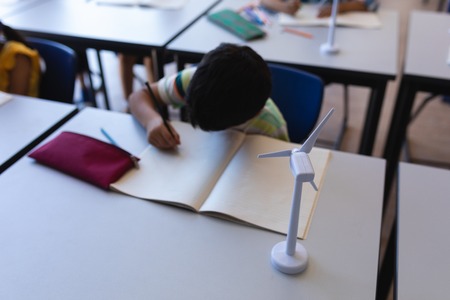 High angle view of schoolboy writing on notebook at desk in classroom of elementary school