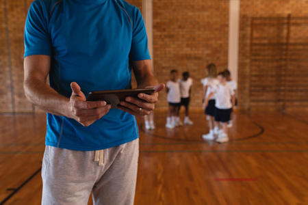 Mid section of basketball coach using digital tablet at basketball court in schoolの写真素材