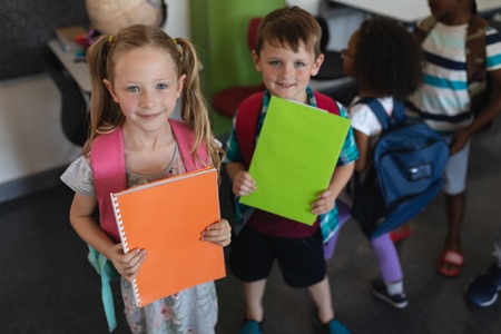 Front view of Caucasian schoolkids holding notebooks and looking at camera in classroom of elementary schoolの写真素材