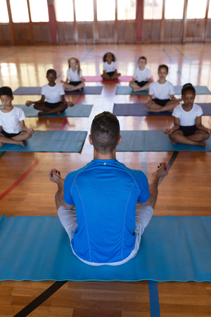 High angle view of yoga teacher teaching yoga to school kids in schoolの写真素材
