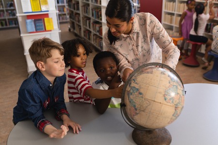 Front view of female teacher teaching the kids about the globe at table in school library