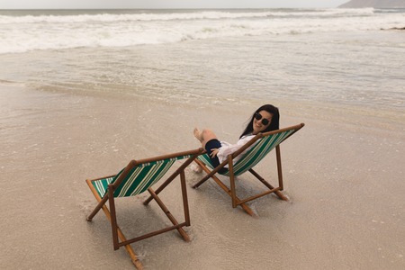 Rear view of beautiful young woman relaxing on sun lounger and looking at camera on beachの写真素材