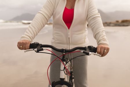 Mid section of senior woman riding a bicycle on the beach against mountains in the backgroundの写真素材