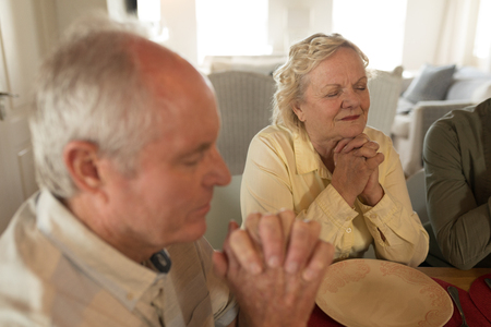 Side view of senior couple praying together before having meal on dining table at homeの写真素材