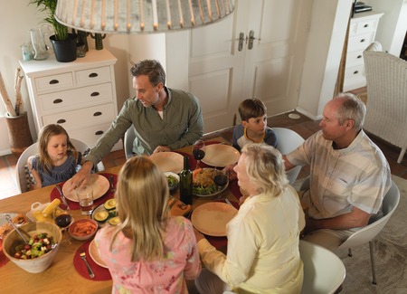 rear view of a multi-generation family interacting with each other while having meal on dining table...
